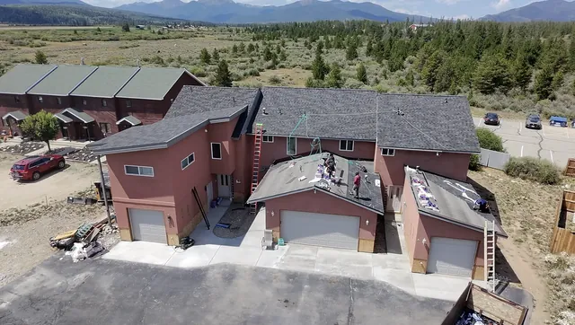 Aerial view of a Rondeau Construction crew re-roofing a multi-unit building in Grand County, Colorado, with shingle bundles staged across the roof