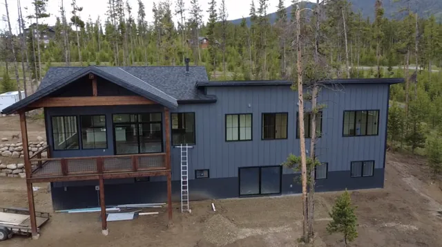 Dark blue board-and-batten custom home with a timber-frame covered deck, set among the pines in Grand County, Colorado, built by Rondeau Construction