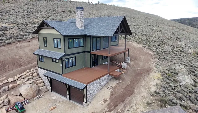 Green custom mountain home with cedar garage doors, stone base, timber-frame entry gable, and composite decks, built by Rondeau Construction in Grand County, Colorado