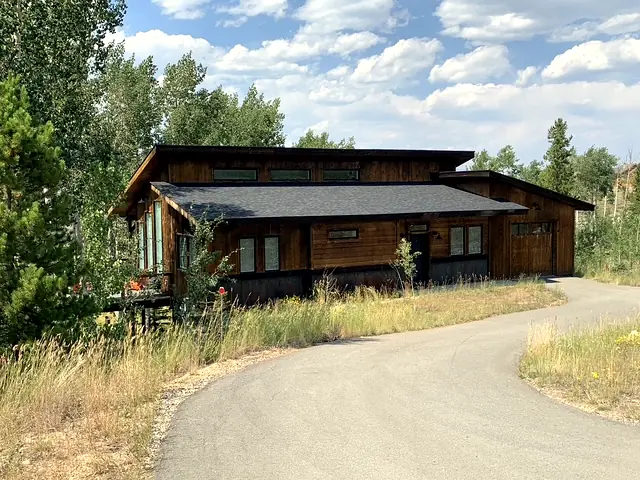 Modern single-level dark cedar home with curved paved driveway among aspens