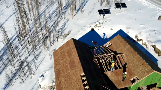 Roof sheathing installation on a mountain cabin with solar panels in winter